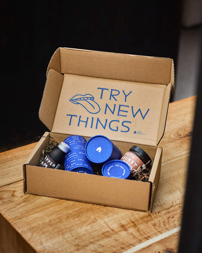 Open cardboard box with 'Try New Things' message on a wooden surface