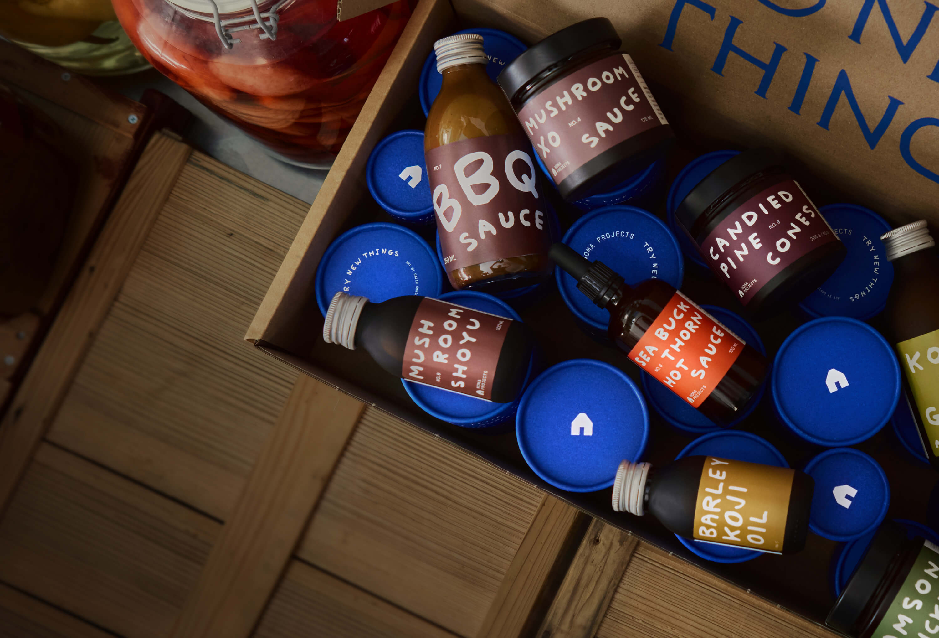 Assorted condiment bottles in a cardboard box on a wooden surface