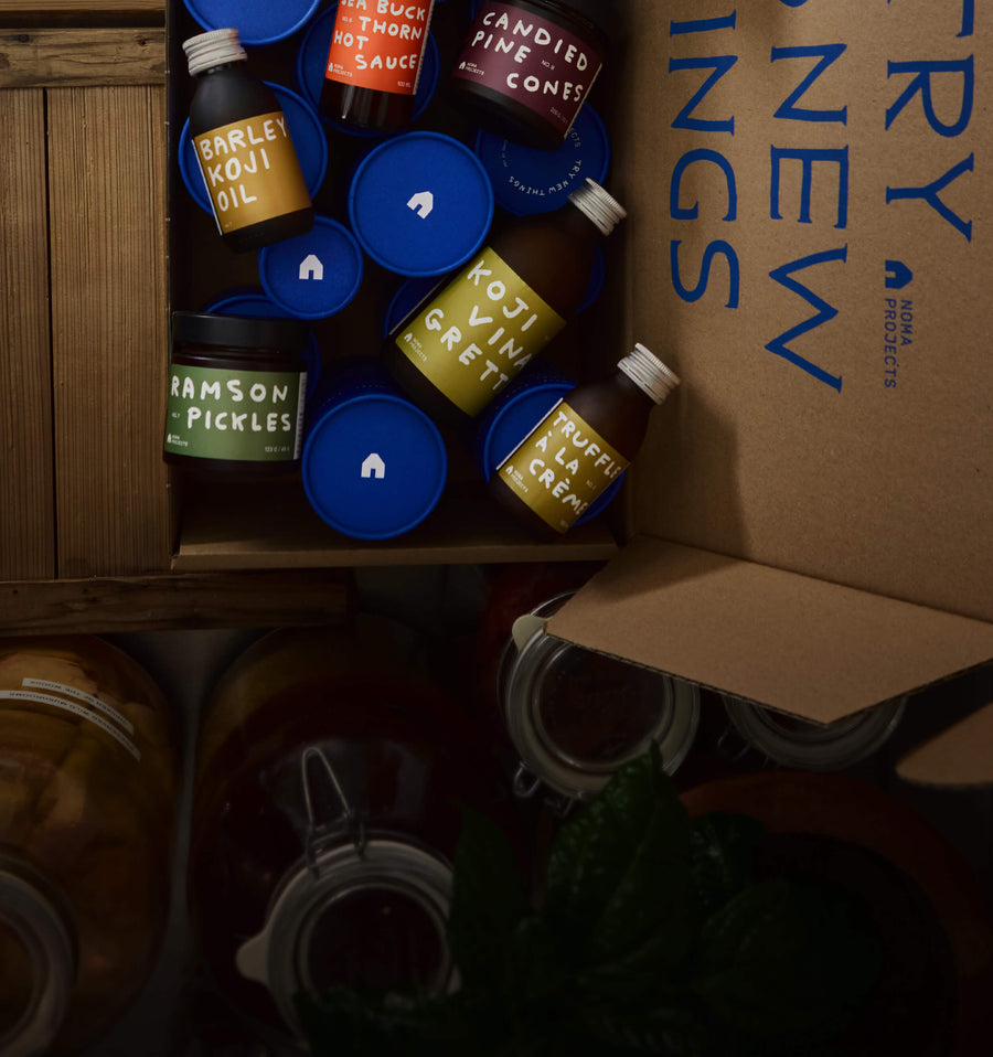 Assorted food products including pickles and oils in a box with 'New York' branding.